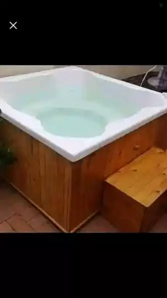 Square wooden hot tub with white interior filled with water
