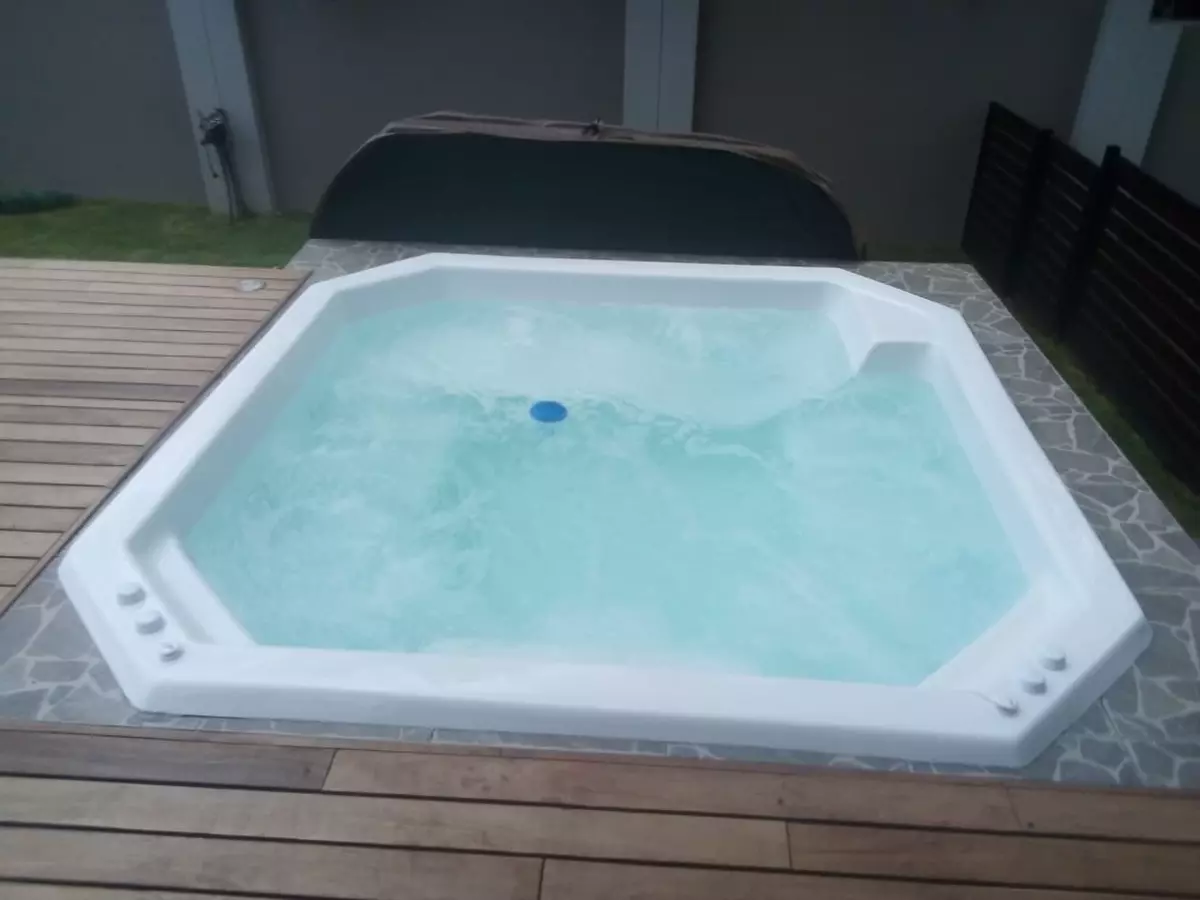 White hexagonal hot tub filled with bubbling water on a stone and wood patio