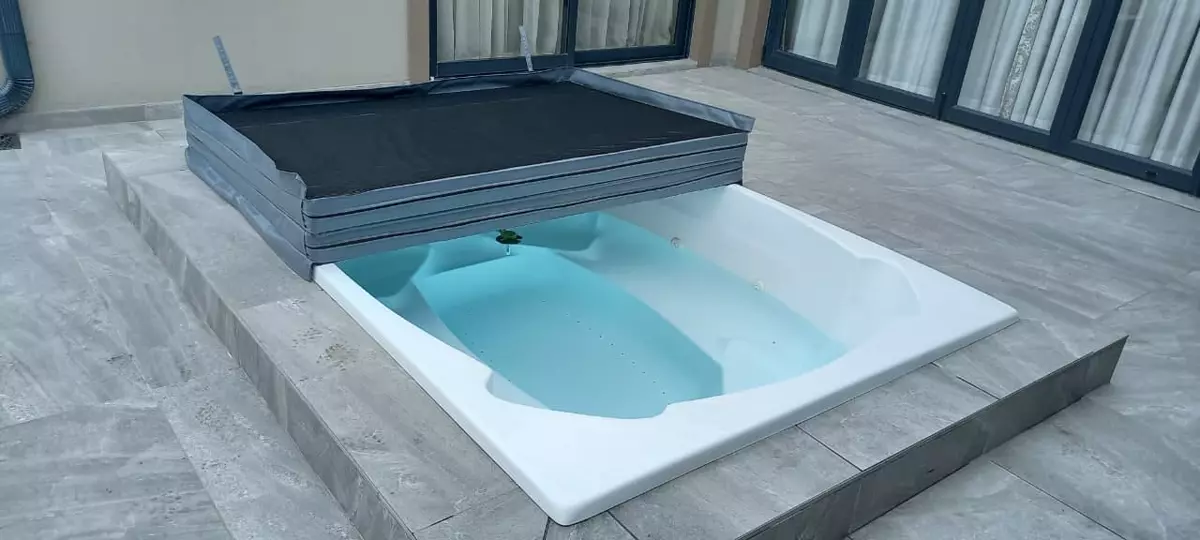 Outdoor hot tub with a folding cover on a grey tiled patio