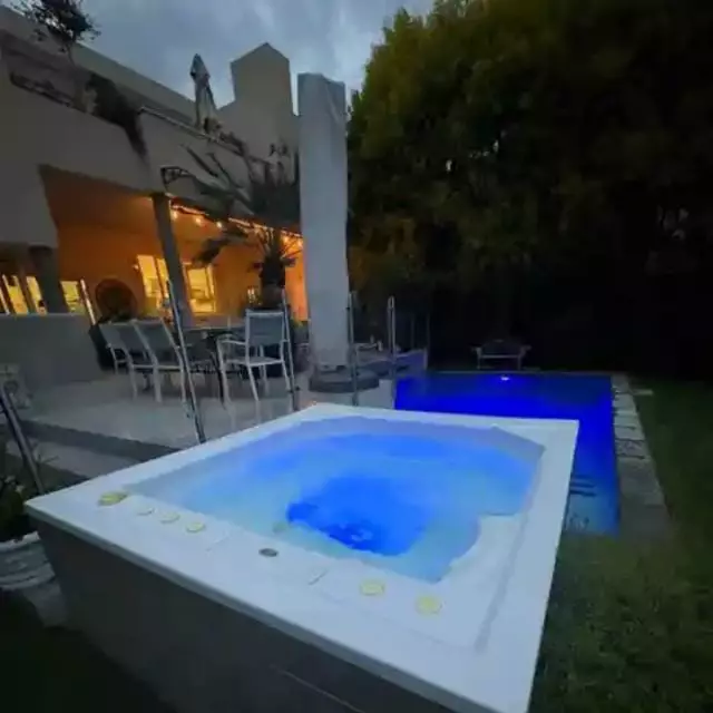 Backyard patio with illuminated hot tub and pool at dusk