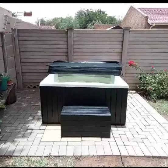 Outdoor hot tub on a paved patio against a wooden fence
